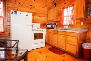 Cocina de cabaña de madera con refrigerador, estufa, microondas y alacenas de madera.