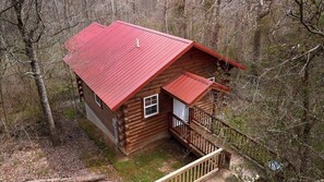 A wooden cabin with a red roof, a small porch, and a window.