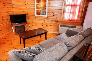 A wooden interior with a sofa, a table, a television, and an air conditioning unit.