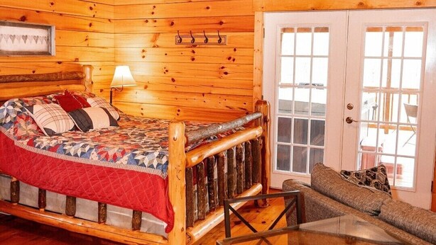 A log cabin interior with a bed, a table, and a sofa. - Lazy Lane Cabins - Buckeye (Logan)