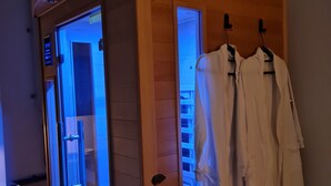 A sauna with glass doors, wooden panels, and towels hanging on hooks. - Spa, sauna, tropical rain sky, complimentary bottle, romantic night  (Macon)