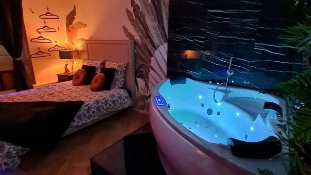 A modern bedroom with a large bed, a sitting area, and a hot tub. - Spa, sauna, tropical rain sky, complimentary bottle, romantic night  (Macon)