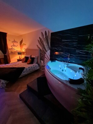 A modern bedroom with a large bed, a sitting area, and a hot tub. - Spa, sauna, tropical rain sky, complimentary bottle, romantic night  (Macon)
