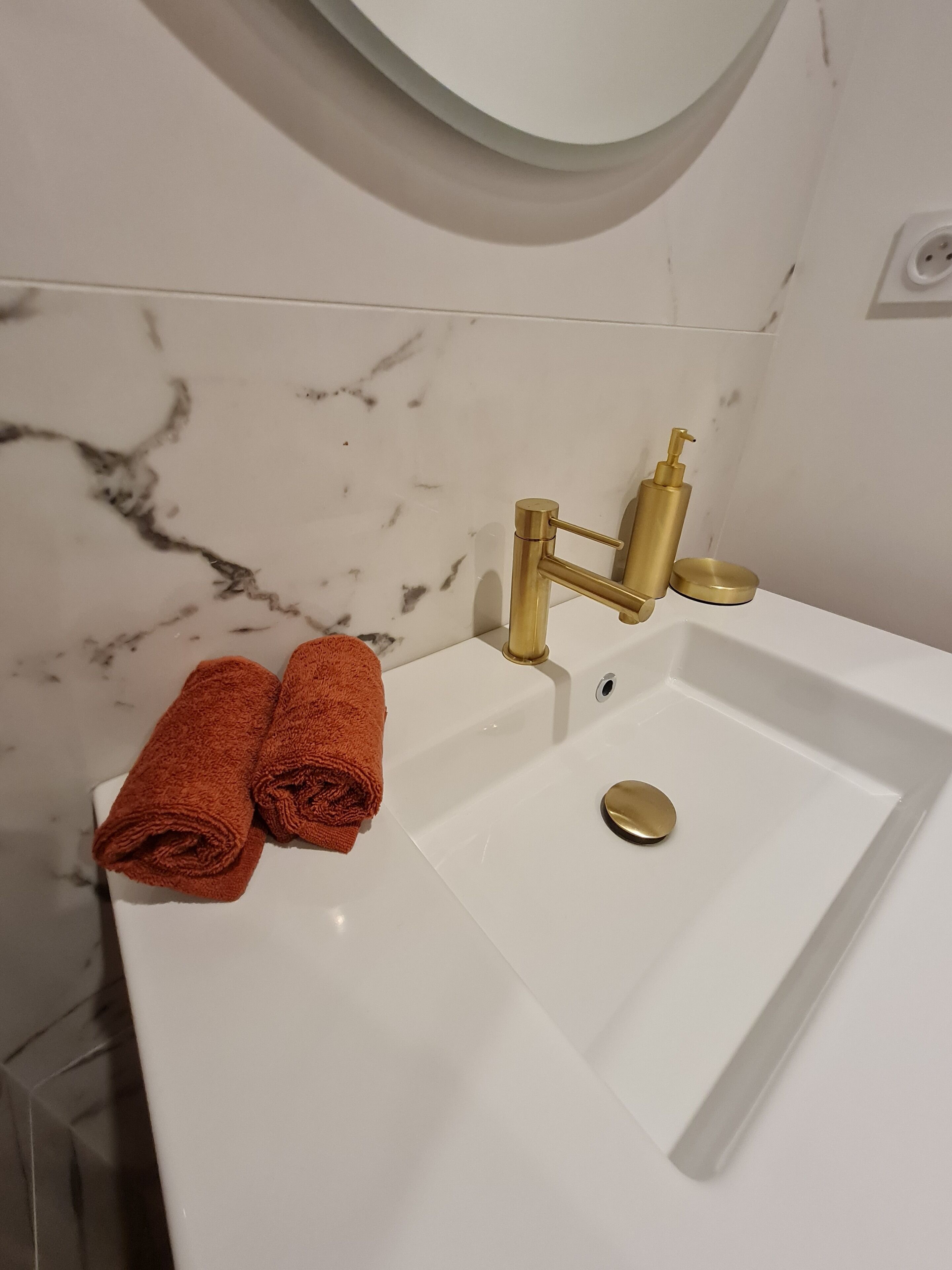 Un baño con lavamanos blanco, grifos dorados y una salpicadera de mármol.