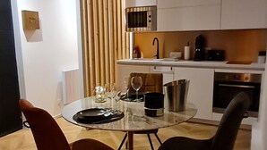 A modern kitchen with white cabinets, a microwave, and a coffee maker. There is a dining table with two chairs and a glass top. - Spa, sauna, tropical rain sky, complimentary bottle, romantic night  (Macon)