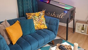 Una sala de estar con un sofá azul, una mesita blanca y un televisor montado en la pared.