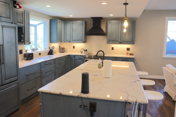 A modern kitchen with grey cabinets, a marble island, and a black range hood.