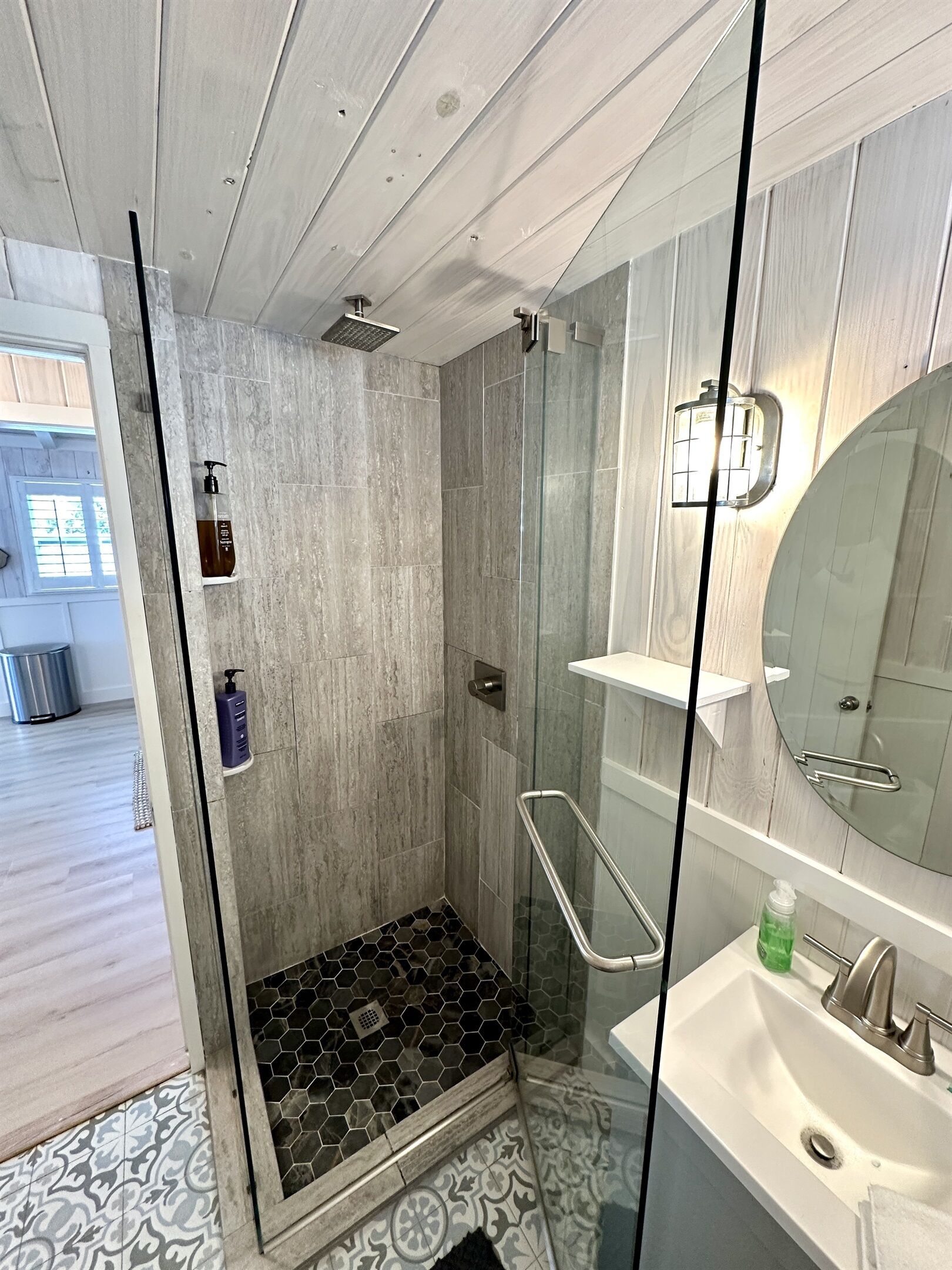 A modern bathroom with a glass shower enclosure, a white sink, and a large mirror.