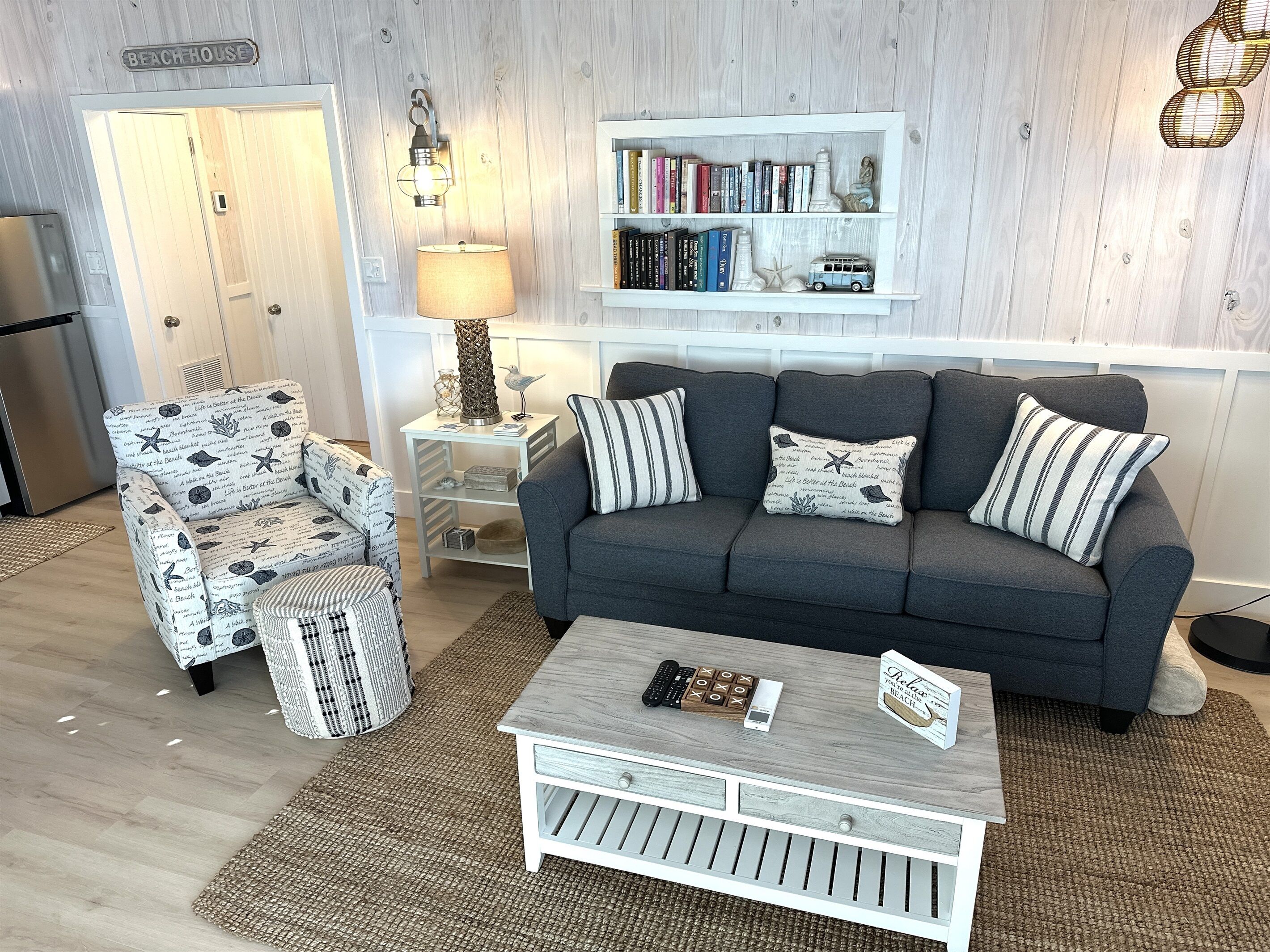 A living room with a grey sofa, striped armchair, and a coffee table with a remote control and a card.