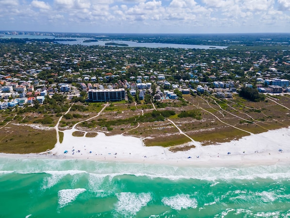 An aerial view of a coastal area with a beach, residential buildings, and a large hotel complex.