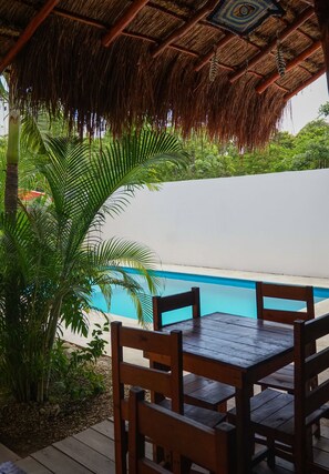 A wooden table and chairs under a thatched roof, overlooking a pool. - hotel stella maris tulum (Tulum)
