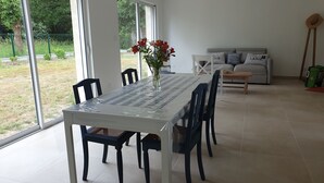 A dining area with a table and chairs, a vase with flowers, and a sofa with cushions. - New house 5 minutes from the beach and customs path (Mesquer)