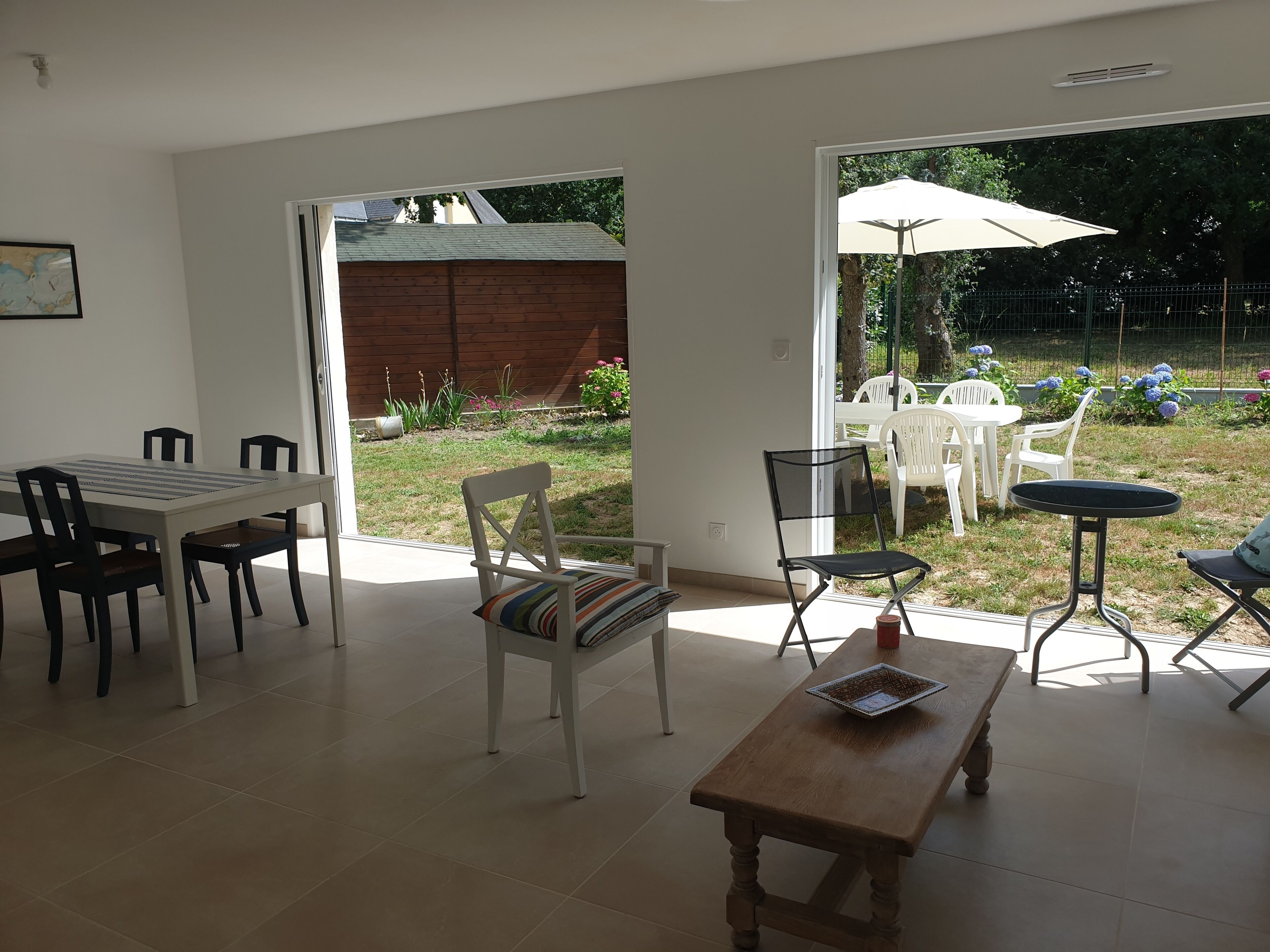 A spacious living area with a dining table, chairs, a wooden coffee table, and a sliding glass door leading to a garden.