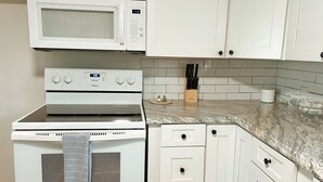 Uma cozinha com micro-ondas, fogão e armários brancos.