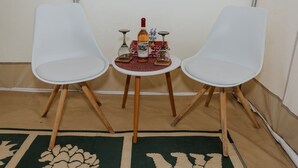 Zwei weiße Stühle mit Holzbögen, ein kleiner runder Tisch mit einer Flasche und zwei Gläsern sowie eine dekorative Schachtel auf einem beigefarbenen Teppich.