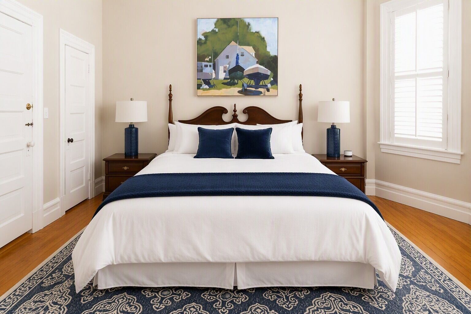 A bedroom with a large bed, two bedside tables with lamps, a painting on the wall, and a patterned rug.