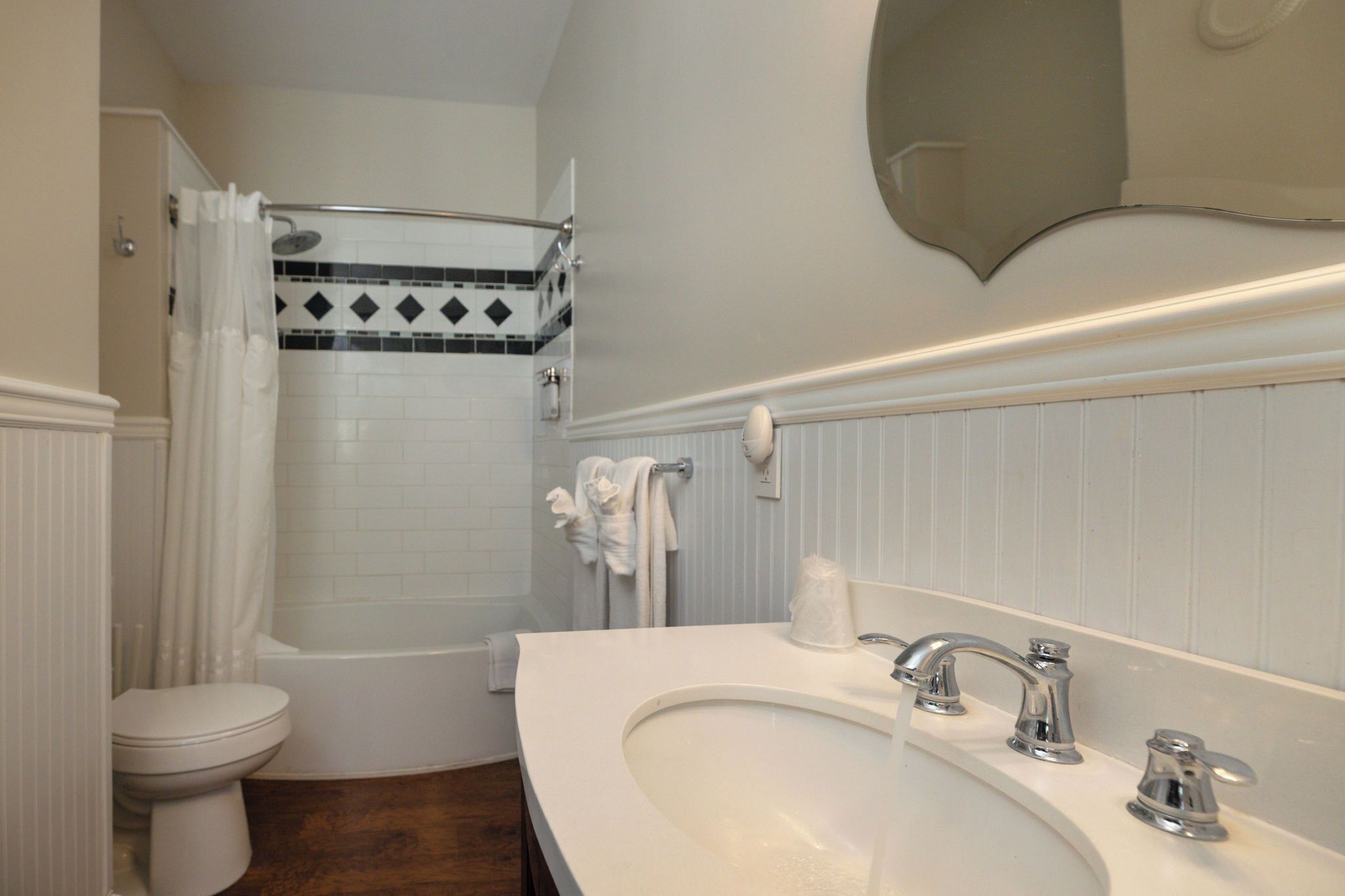 A bathroom with a white sink, two faucets, a toilet, a shower with a curtain, and a tiled wall.