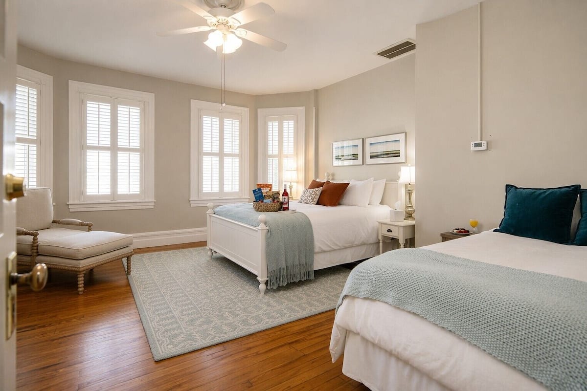 A bedroom with two beds, a chair, a nightstand, a ceiling fan, and a window.