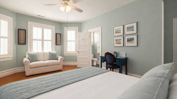 A bedroom with a bed, a desk, a chair, a ceiling fan, and a window.