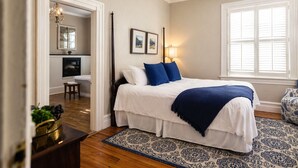 A bedroom with a bed, a nightstand, a chair, a desk, a mirror, and a window. - The Edenton Collection-Captain's Quarters Inn (Edenton)