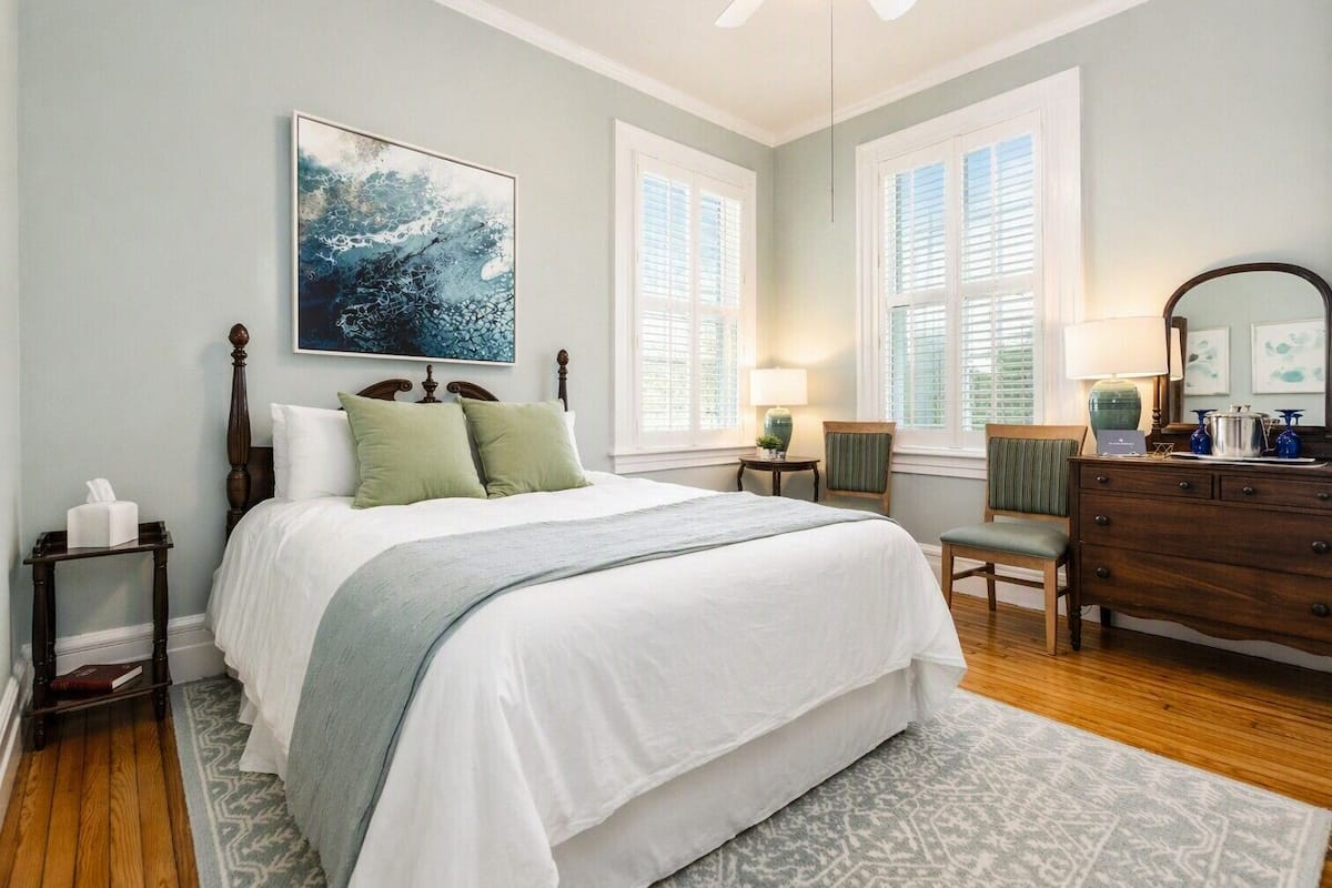 A bedroom with a bed, two nightstands, a dresser, and a large window with blinds.