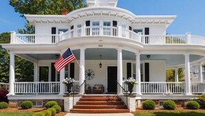 A white, two-story house with a balcony, a flag, and a compass on the front porch. - The Edenton Collection-Captain's Quarters Inn (Edenton)