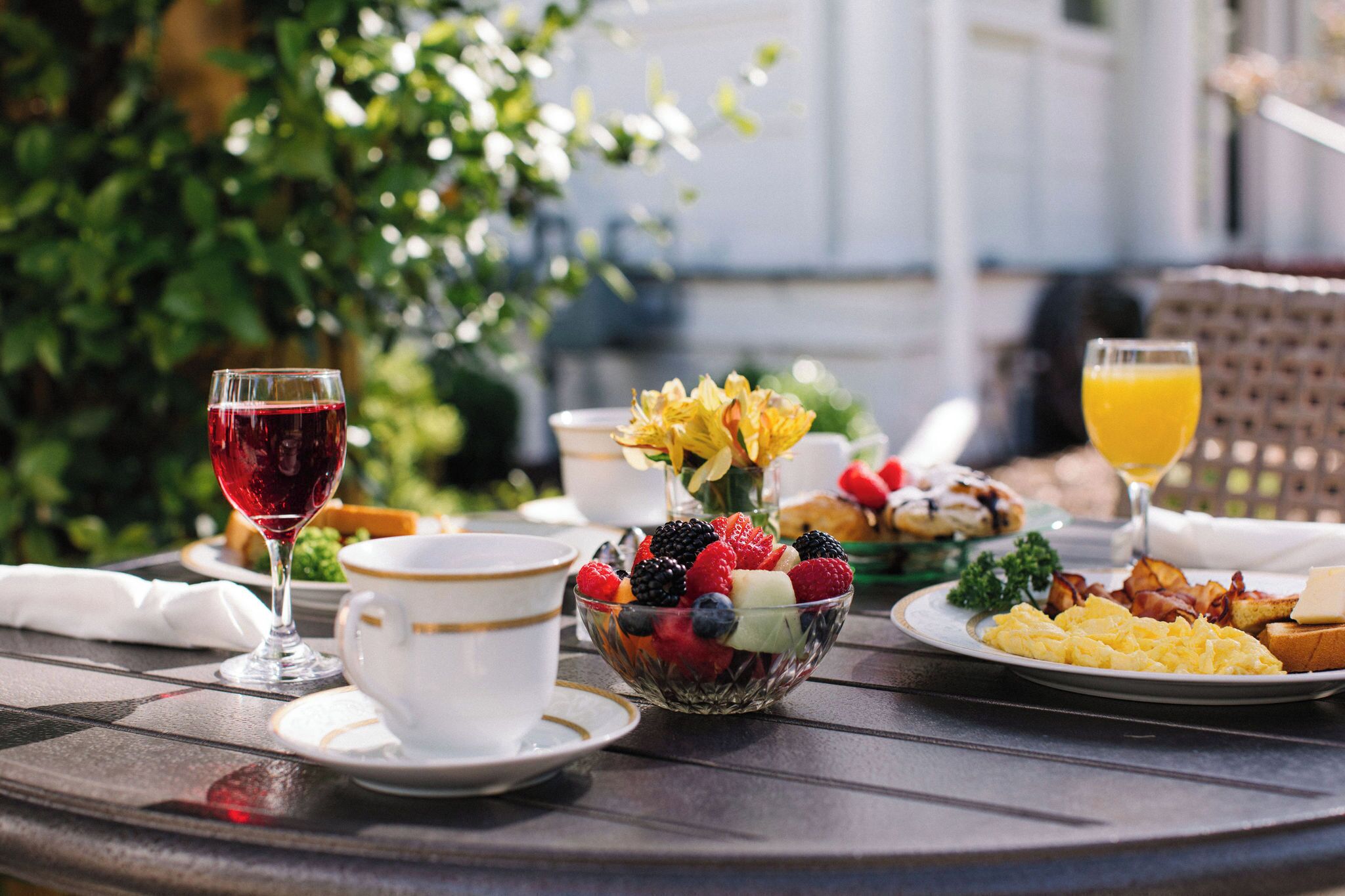 A breakfast table with a fruit bowl, a glass of red wine, a cup, and a plate of scrambled eggs.
