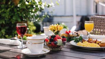 A breakfast table with a fruit bowl, a glass of red wine, a cup, and a plate of scrambled eggs.