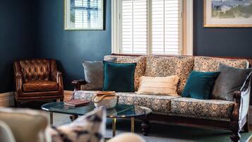 A living room with a patterned sofa, a leather armchair, and a glass coffee table.