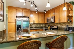 Una cocina con armarios de madera, electrodomésticos de acero inoxidable, encimeras de granito y sillas de mimbre.