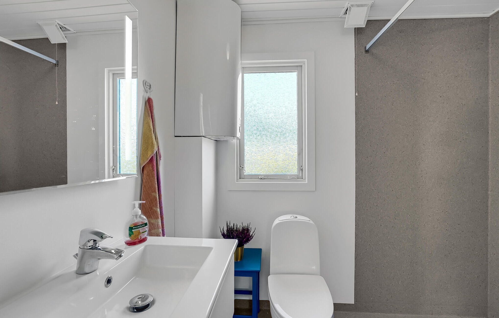 Ein Badezimmer mit weißem Waschbecken, Toilette, Fenster und Spiegel.