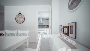 A modern kitchen with white cabinetry, a dining area with white chairs, and a clock on the wall. - PUSHE Village Playa Granada Beach & Golf 2 (Motril)