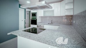 A modern kitchen with white cabinetry, a built-in stove, and granite countertops. - PUSHE Village Playa Granada Beach & Golf 2 (Motril)