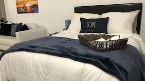 Un lit bien fait, recouvert d’une couverture bleu foncé, avec un panier en osier posé dessus.