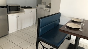 Une cuisine compacte équipée d’un four à micro-ondes, d’un évier et de placards. On y trouve également une table à manger avec des assiettes et un verre.