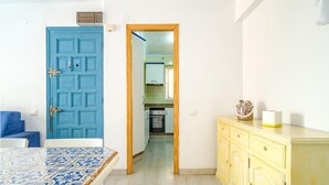 A room with a blue door, a bed with a patterned cover, a yellow dresser, and a view into a kitchen area. - 3 bedroom cozy apartment in Sueca (Sueca)