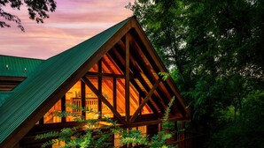 Une cabane en rondins avec un toit à forte pente, de grandes fenêtres et entourée d’une végétation luxuriante.