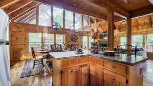Une cabane en bois dotée d’une grande cuisine comprenant un îlot central, des armoires en bois et un coin repas avec des chaises et une table.