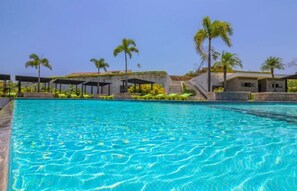 Ein Schwimmbecken mit klarem, blauem Wasser, umgeben von Liegestühlen und Palmen.