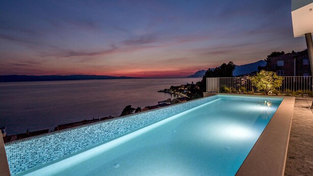 A swimming pool with a view of a sunset over a body of water, surrounded by buildings.