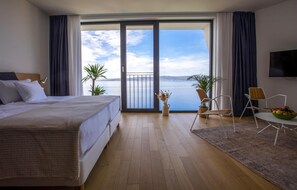 Relax on the balcony overlooking the water with a scenic view, enjoy meals at the small dining table, and unwind in the spacious room with a large bed and flat-screen TV.