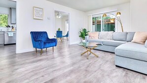 Una sala moderna con un sillón azul, un sofá gris y una mesa de centro de vidrio.