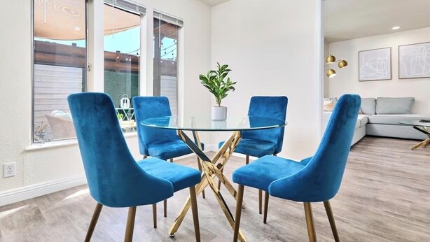 Comedor con mesa de vidrio y sillas azules, una planta en maceta y un sofá al fondo.