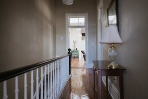 Un couloir avec un plancher en bois, une rambarde blanche et une lampe posée sur une table.