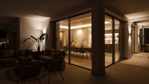 Un salon moderne avec un coin repas, agrémenté d'une cloison en verre, de meubles en osier et d'un éclairage d'ambiance.