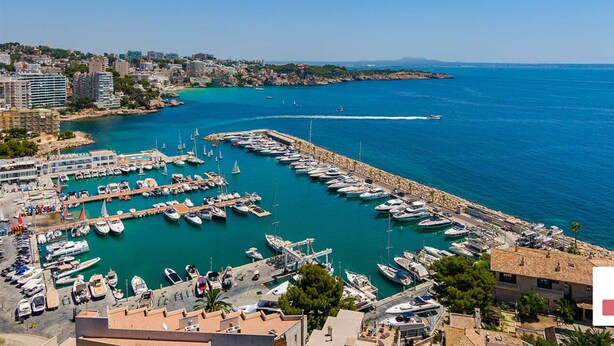 Un port de plaisance où sont amarrés de nombreux bateaux, une mer d’un bleu limpide et des bâtiments qui bordent la côte.