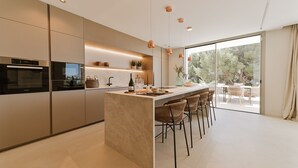 Une cuisine moderne dotée d’un îlot central, de tabourets de bar et donnant sur une terrasse extérieure.