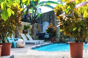A pool area with lounge chairs, a barbecue grill, and potted plants.