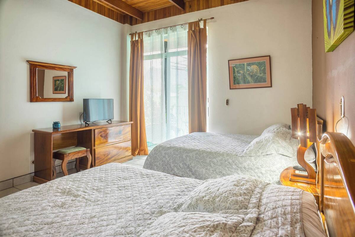 A bedroom with two beds, a wooden dresser, a television, and a painting on the wall.