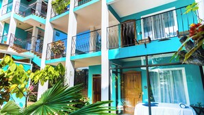 A multi-story hotel with balconies, a glass door entrance, and potted plants. - The Blue Suites & Spa (La Fortuna)